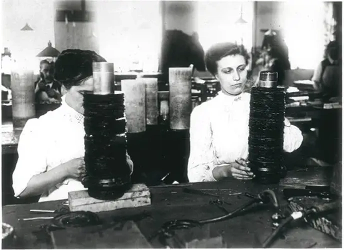Two women sitting at factory workbench coil winding